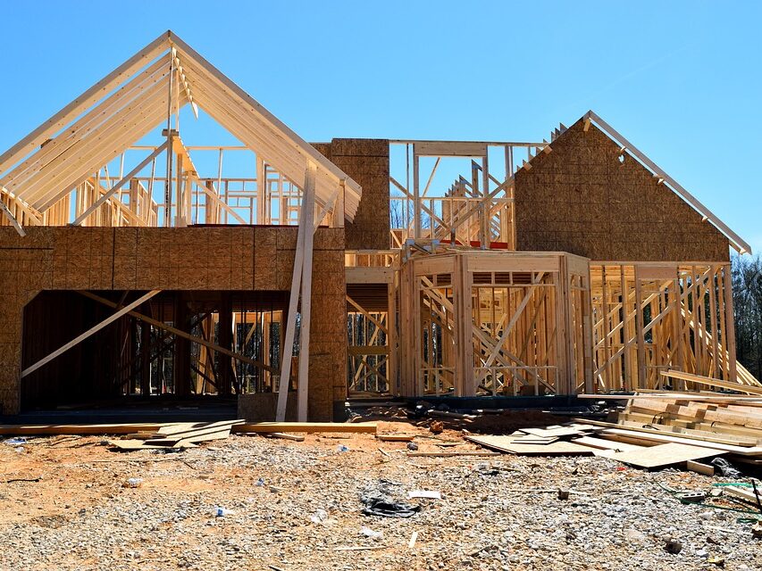 A two-story wood-framed home under construction with partial OSB sheathing and exposed roof trusses